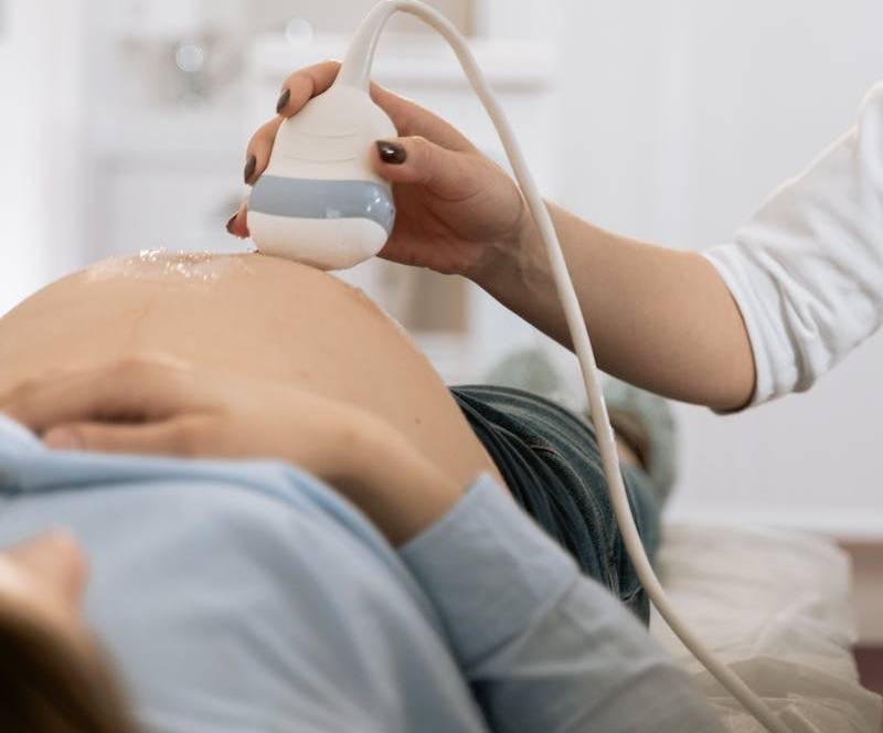 Healthcare professional performing an ultrasound scan on a pregnant woman's abdomen in a clinical setting